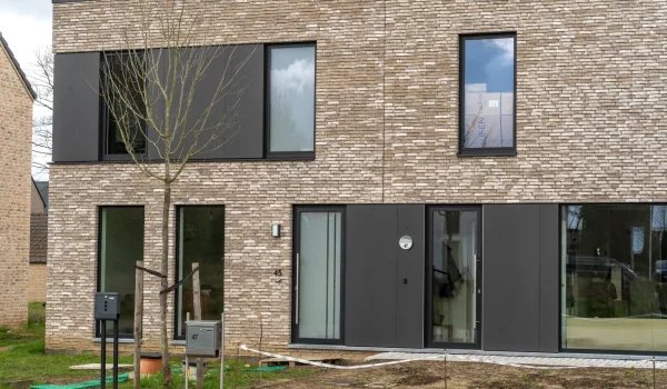 Bakstenen gevel met donkere gevelbekleding rond ramen en deur